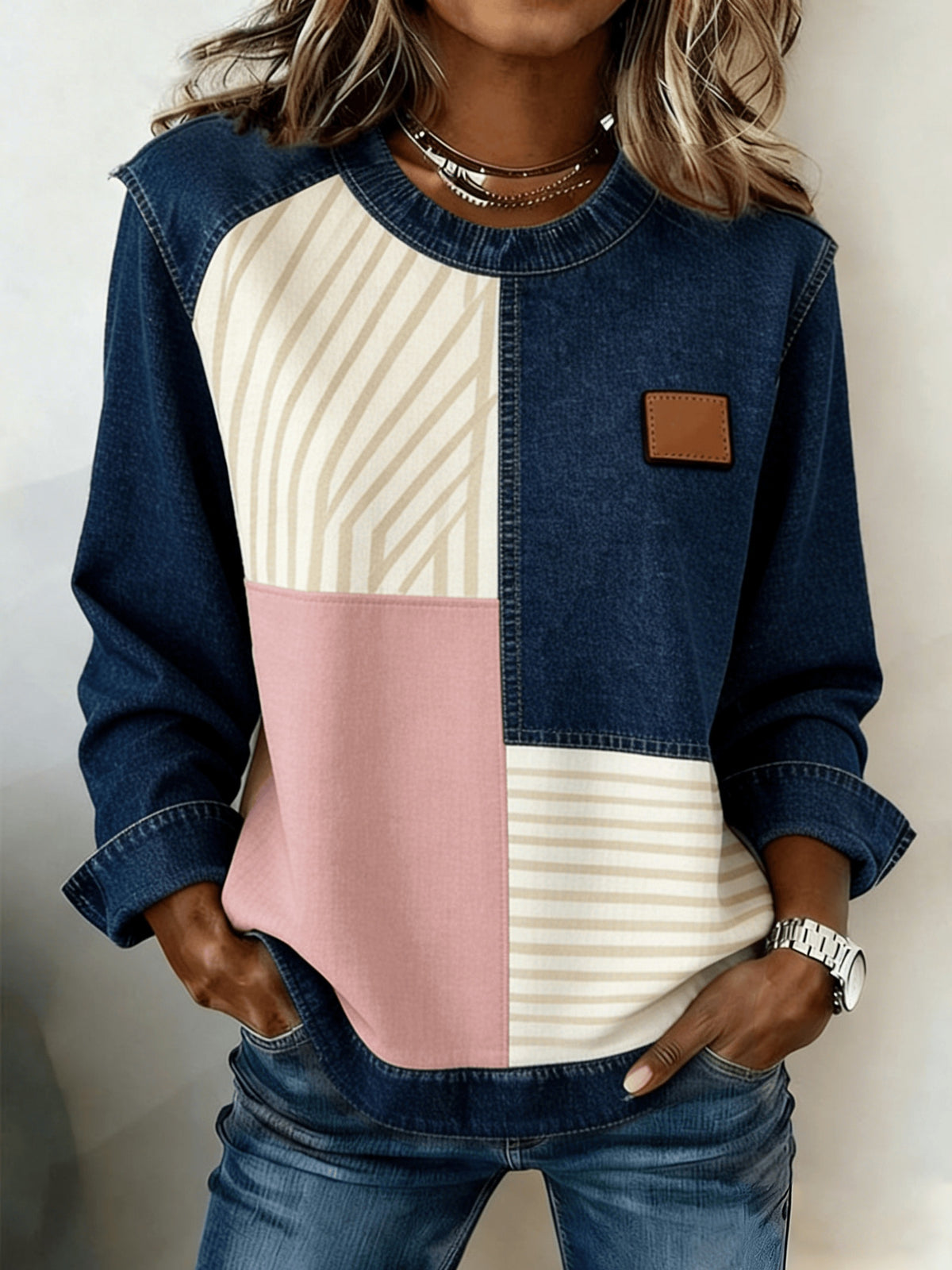 Women's patchwork denim sweatshirt with beige striped and pink color-block panels and a brown leather patch.