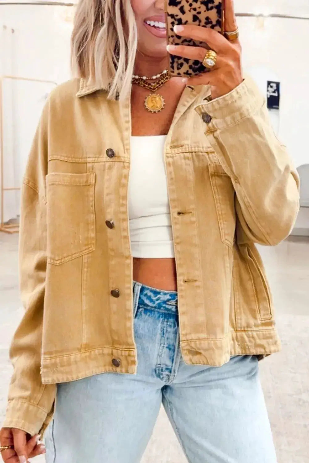 Washed tan cotton-blend denim trucker jacket with metal front buttons, worn over a white crop top