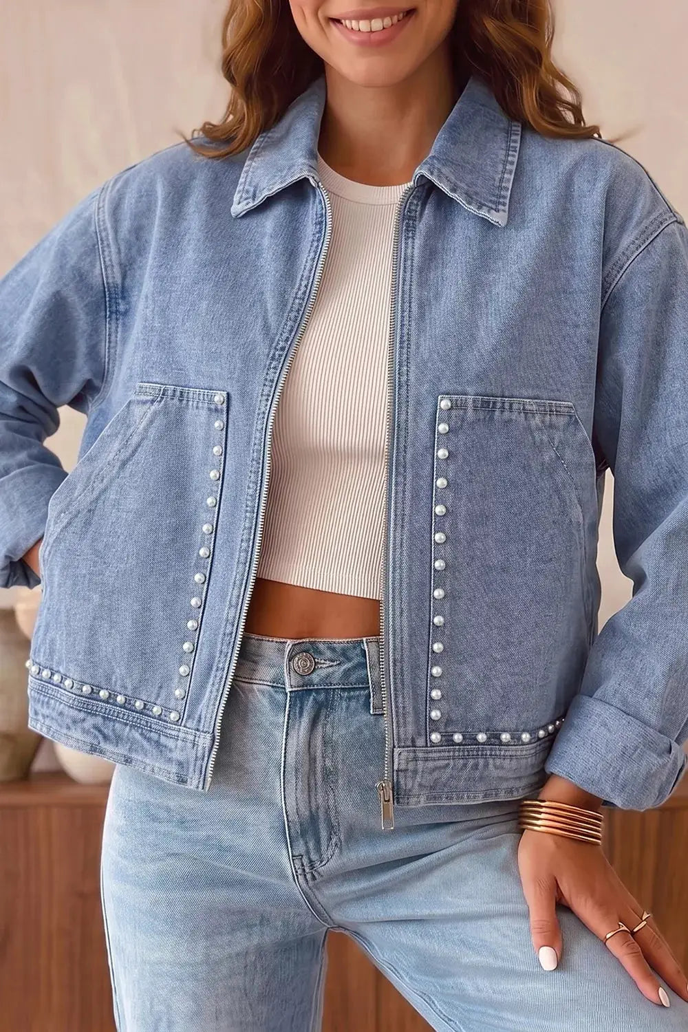 Long sleeve studded denim jacket with metal zipper and rivet pockets in light wash.