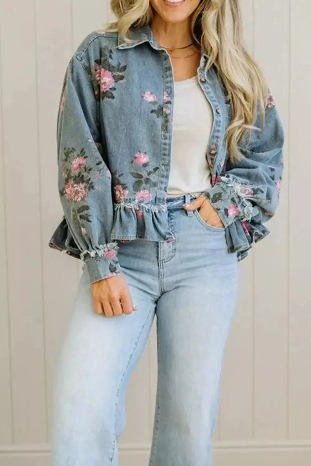 Women’s floral print denim jacket with pink rose pattern and a ruffled hem in light wash.