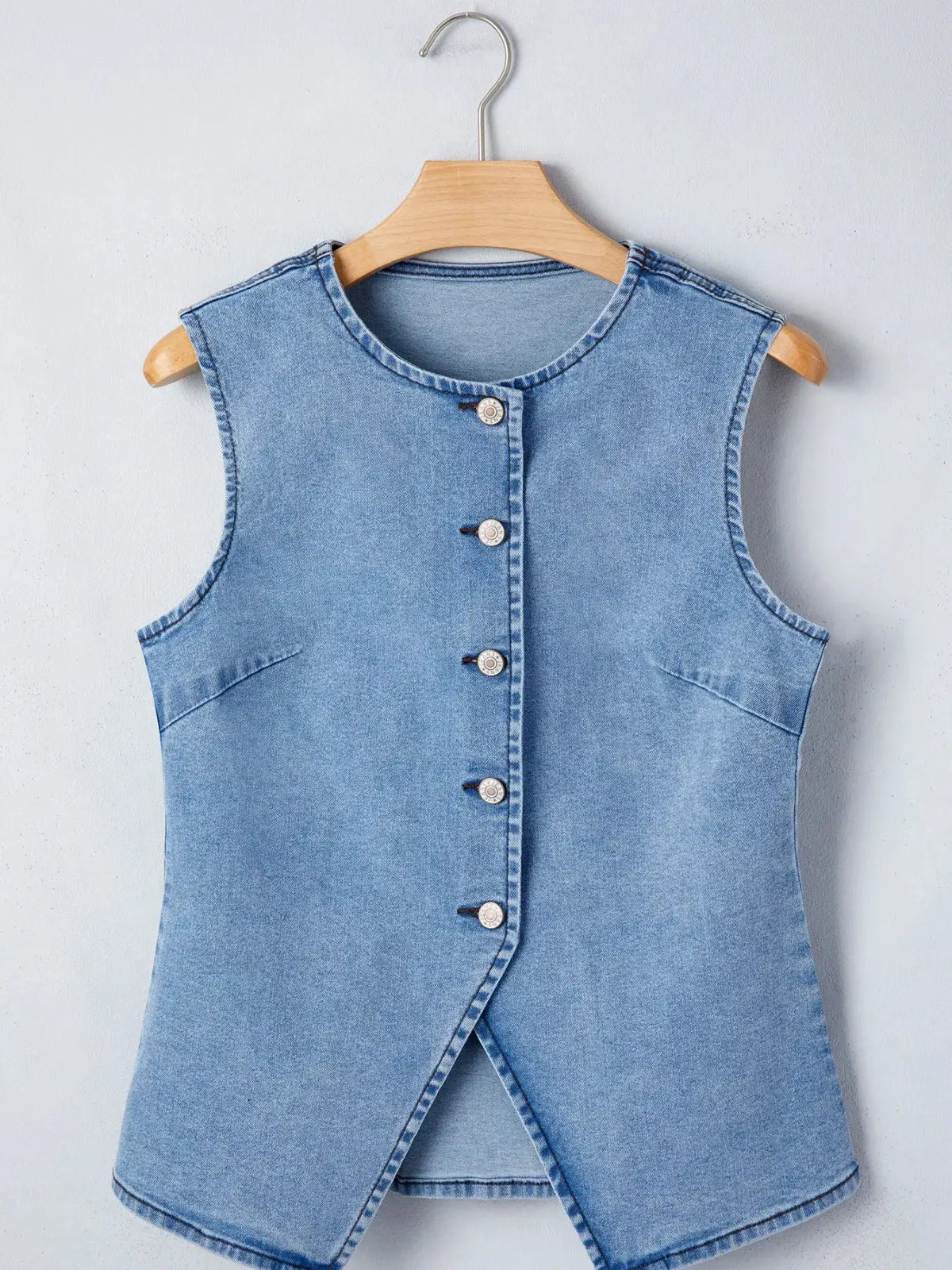 Denim sleeveless vest with front buttons in light blue, on a wooden hanger