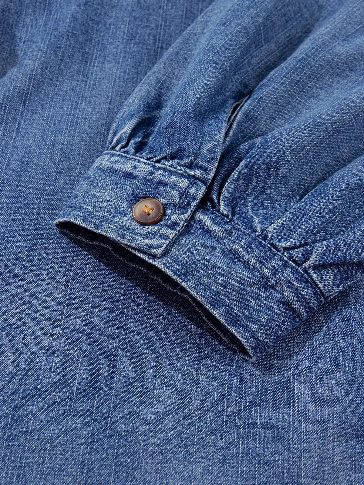 Relaxed blue denim shirt by Trendsi; close-up of sleeve cuff with brown button and visible denim texture