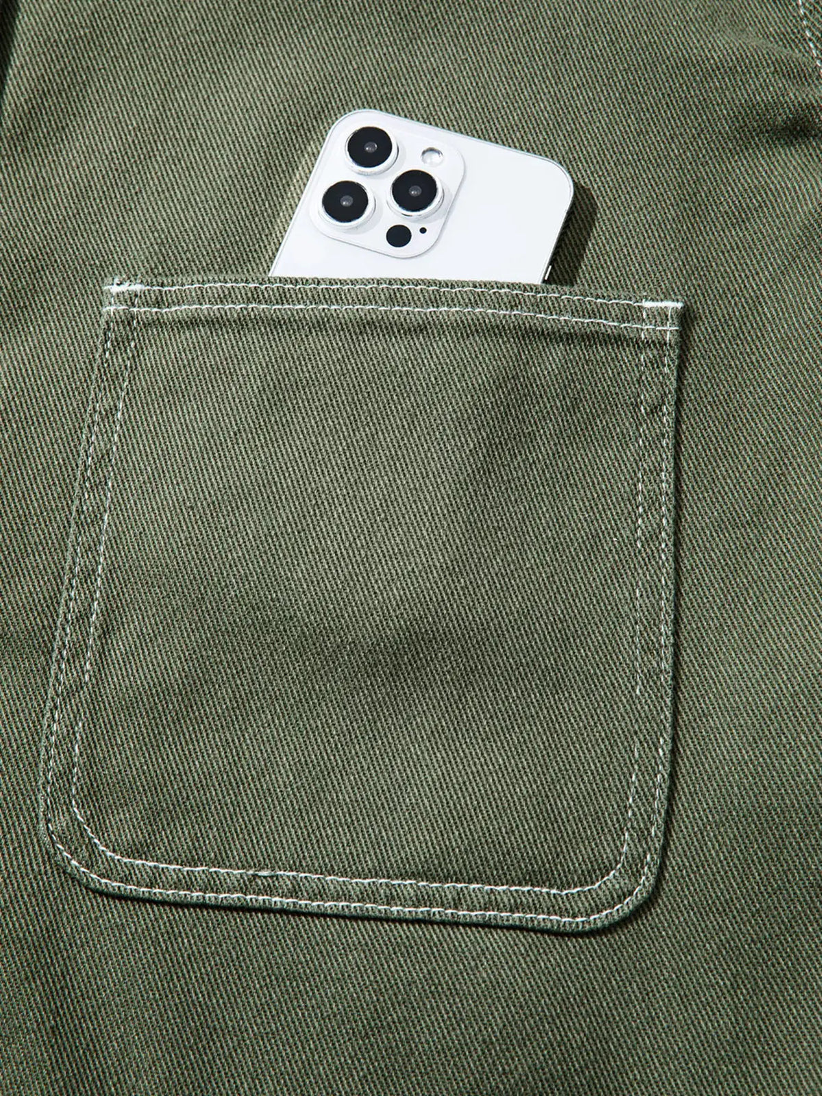 Boyfriend denim jacket pocket in olive denim with white stitching and a white smartphone peeking out.