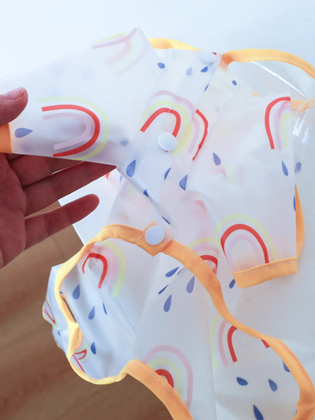 Lightweight waterproof pet raincoat with pastel rainbow print and orange trim, snap buttons.