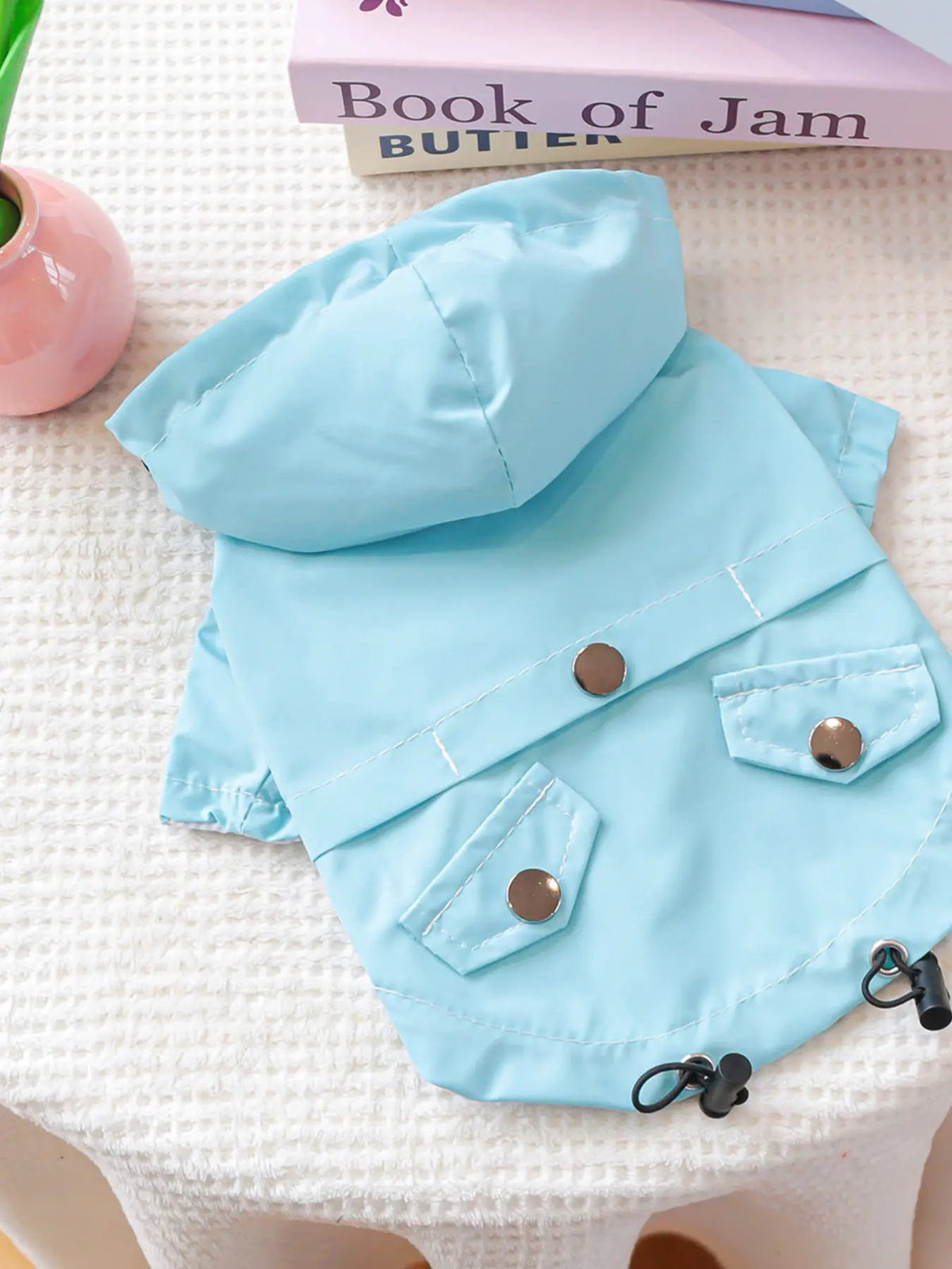 Lightweight waterproof pet raincoat in light blue with hood and metal snap buttons.