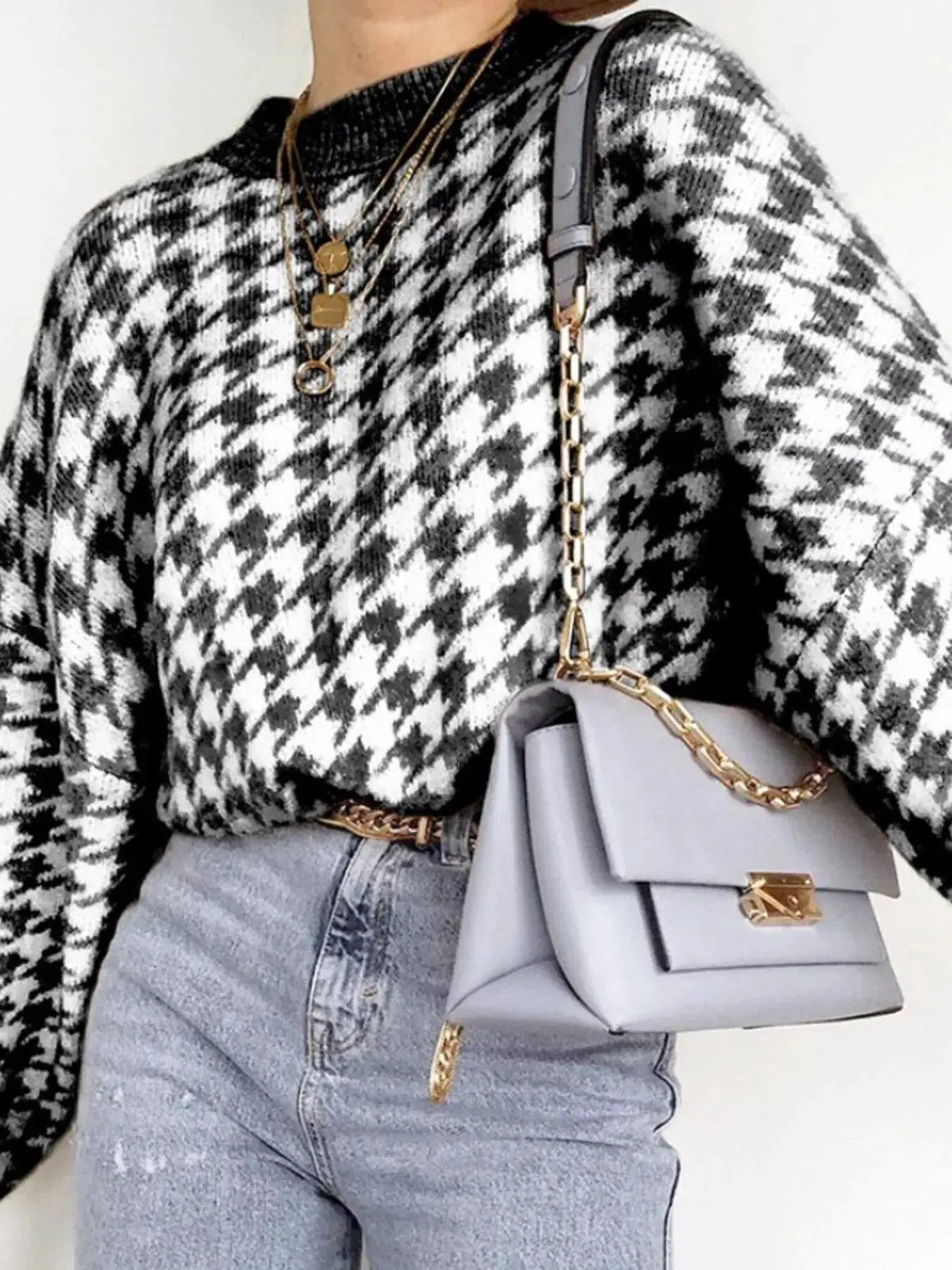 Classic oversized houndstooth knit sweater in black and white, styled with light-wash denim and a gray handbag.