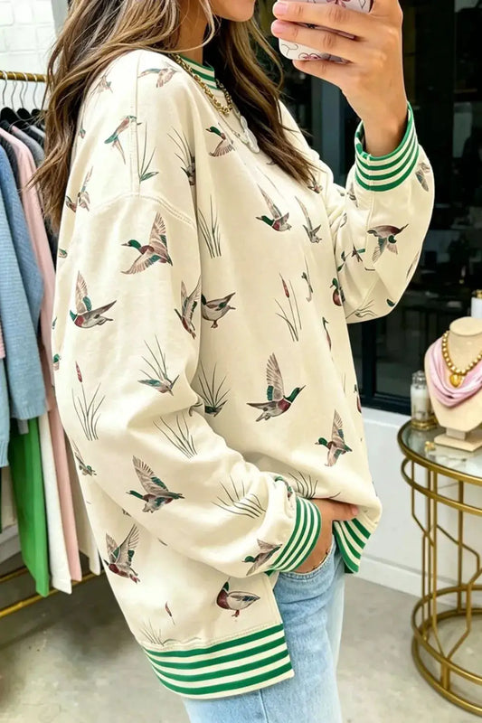 Whimsical duck print sweatshirt in beige with green striped cuffs and hem, casual everyday wear.