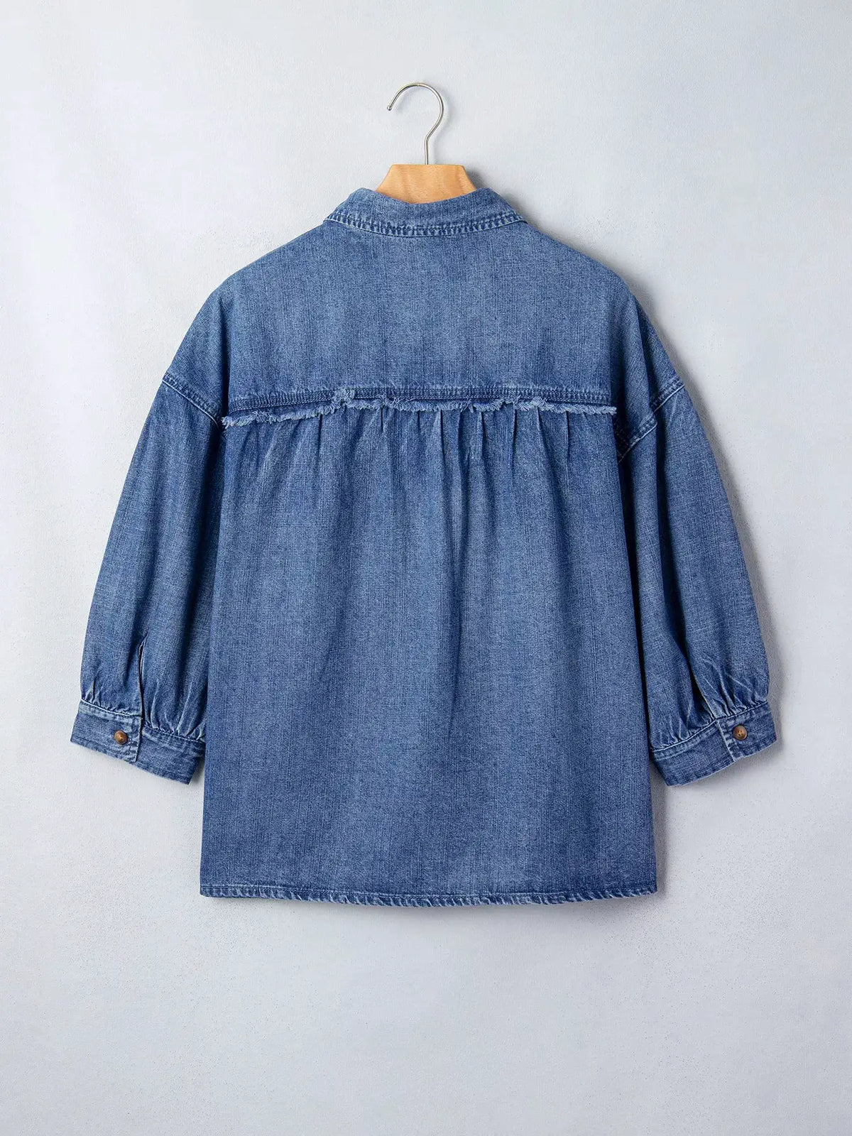 Relaxed denim shirt in light blue on a hanger with gathered back yoke and frayed seam detail