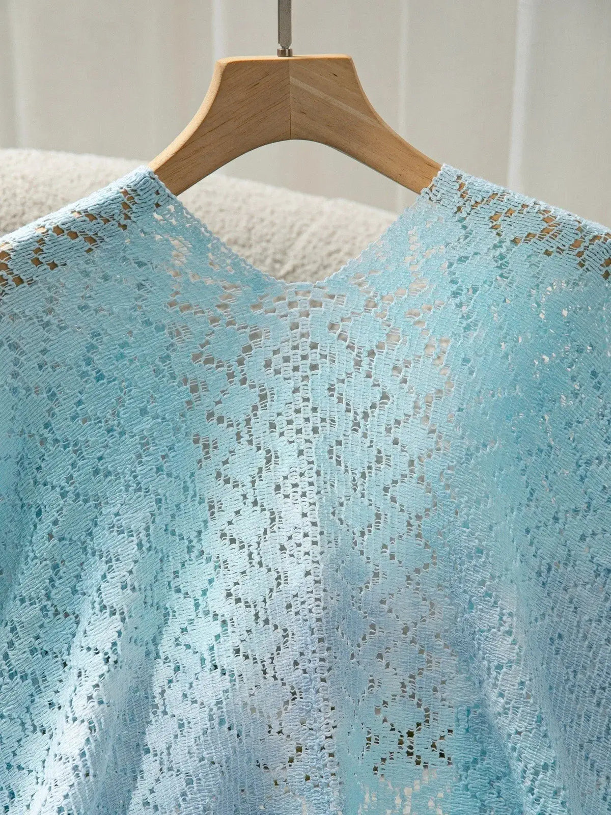 Lightweight gradient openwork knit beach cover up in light blue crochet on a wooden hanger.