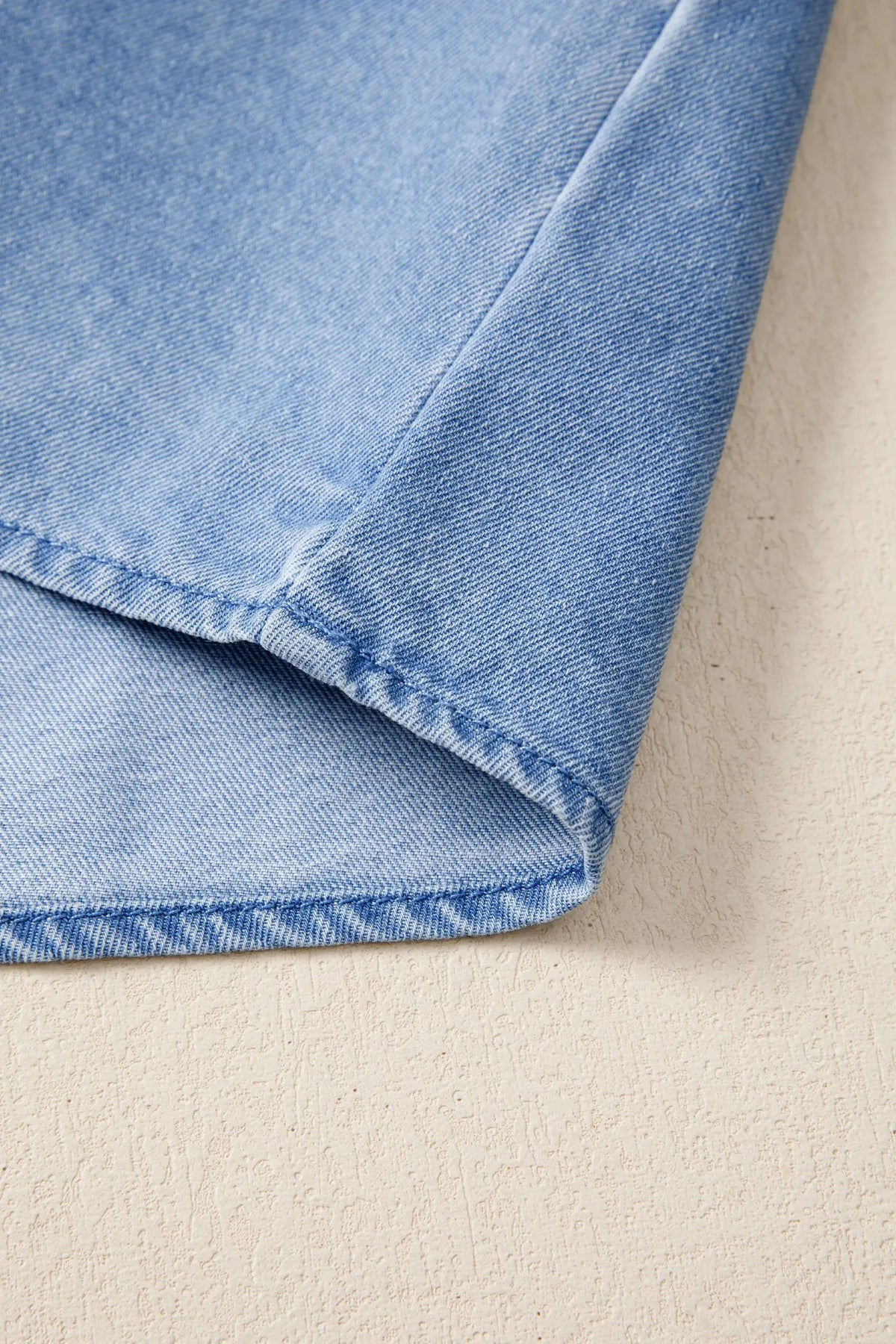 Distressed denim top in light-wash blue; close-up of fabric and seam details