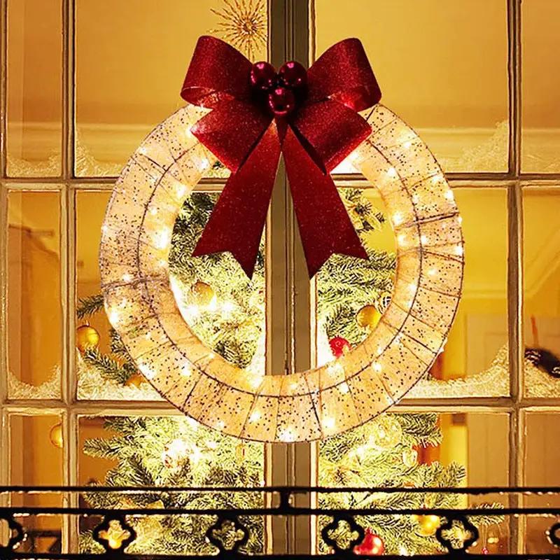 Christmas wreath with warm LED lights on a metal ring, 50 cm, adorned with a large red bow for front door decor.