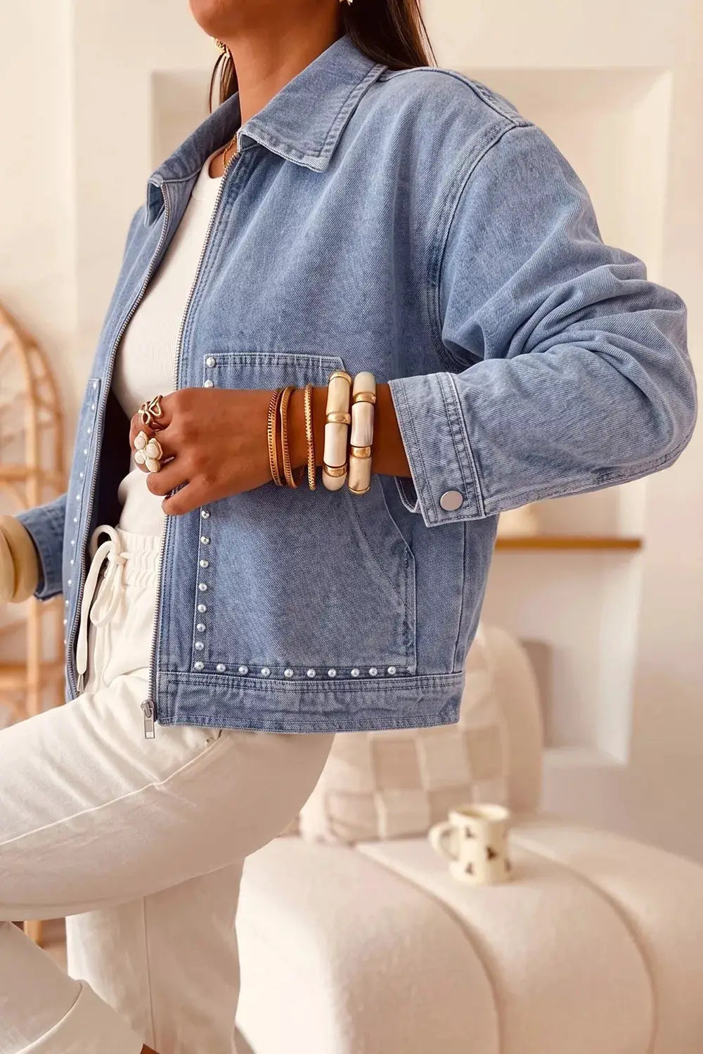 Long-sleeve denim trucker jacket with a metal zipper, studded details and rivet pockets in light blue.