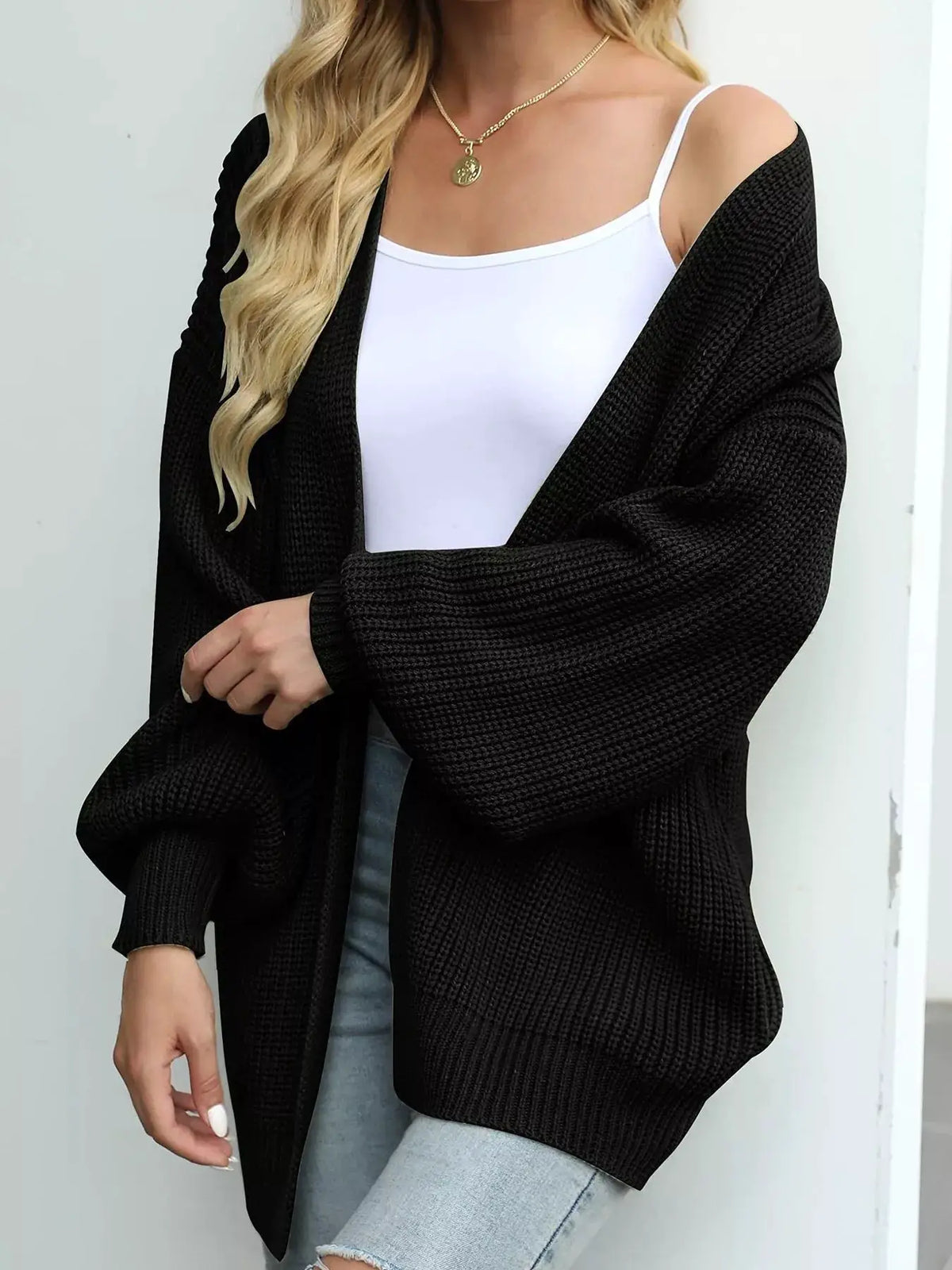 Oversized black chunky knit open-front cardigan with stretch fabric worn over a white tank top.