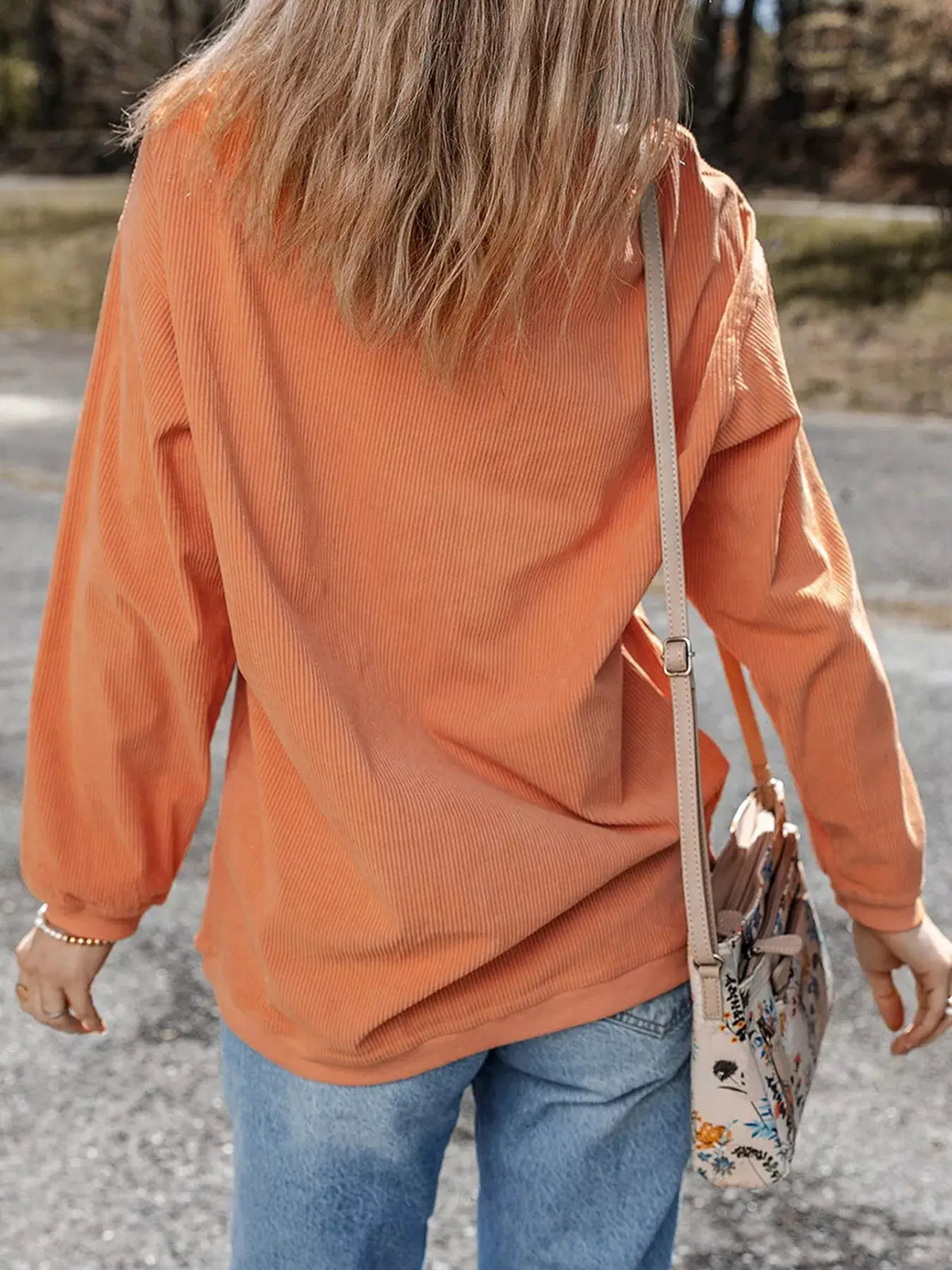 Corded Ribbed Farm Fresh Pumpkins Graphic Sweatshirt in orange, back view with beige crossbody bag.