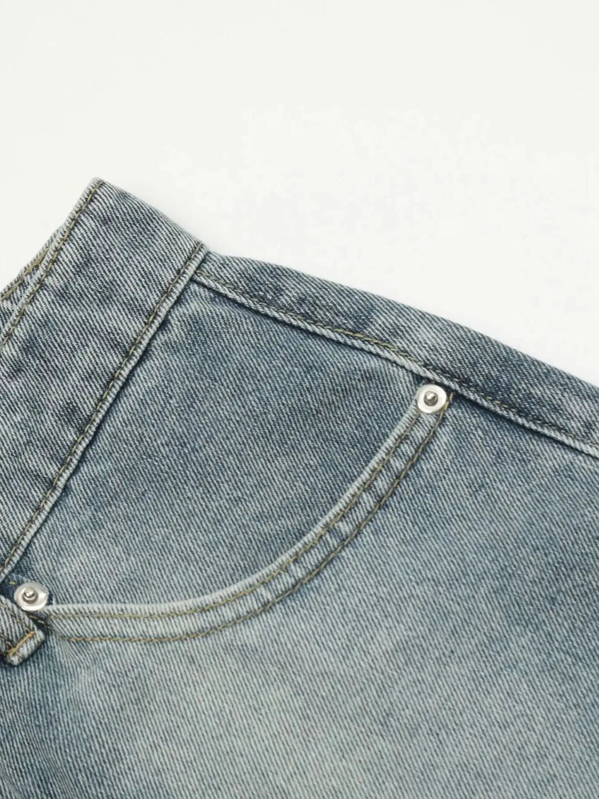 Men's denim shorts fabric close-up in light washed blue with visible stitching and metal rivet.