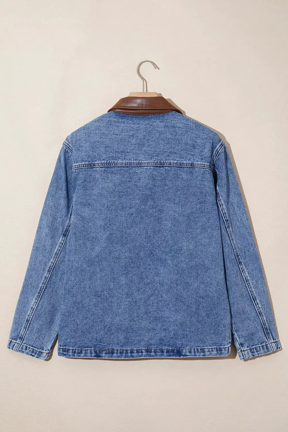 Denim jacket with brown leather collar on hanger; long sleeves, blue wash, back view.
