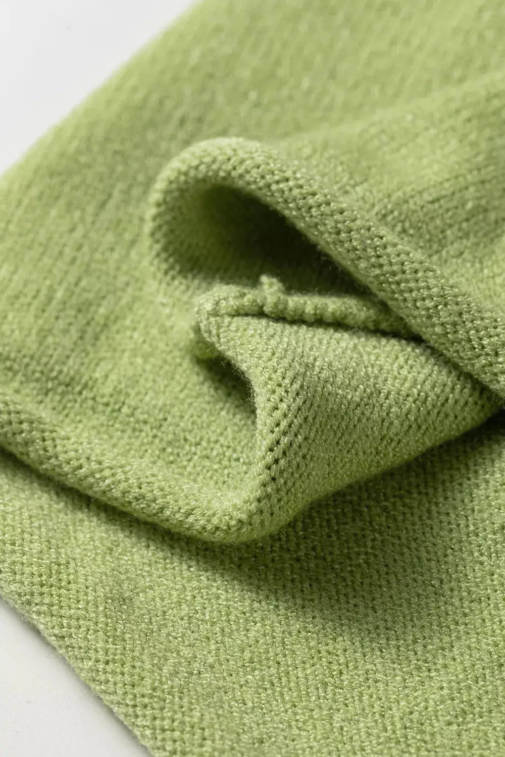Knitted green sweater fabric close-up showing soft texture