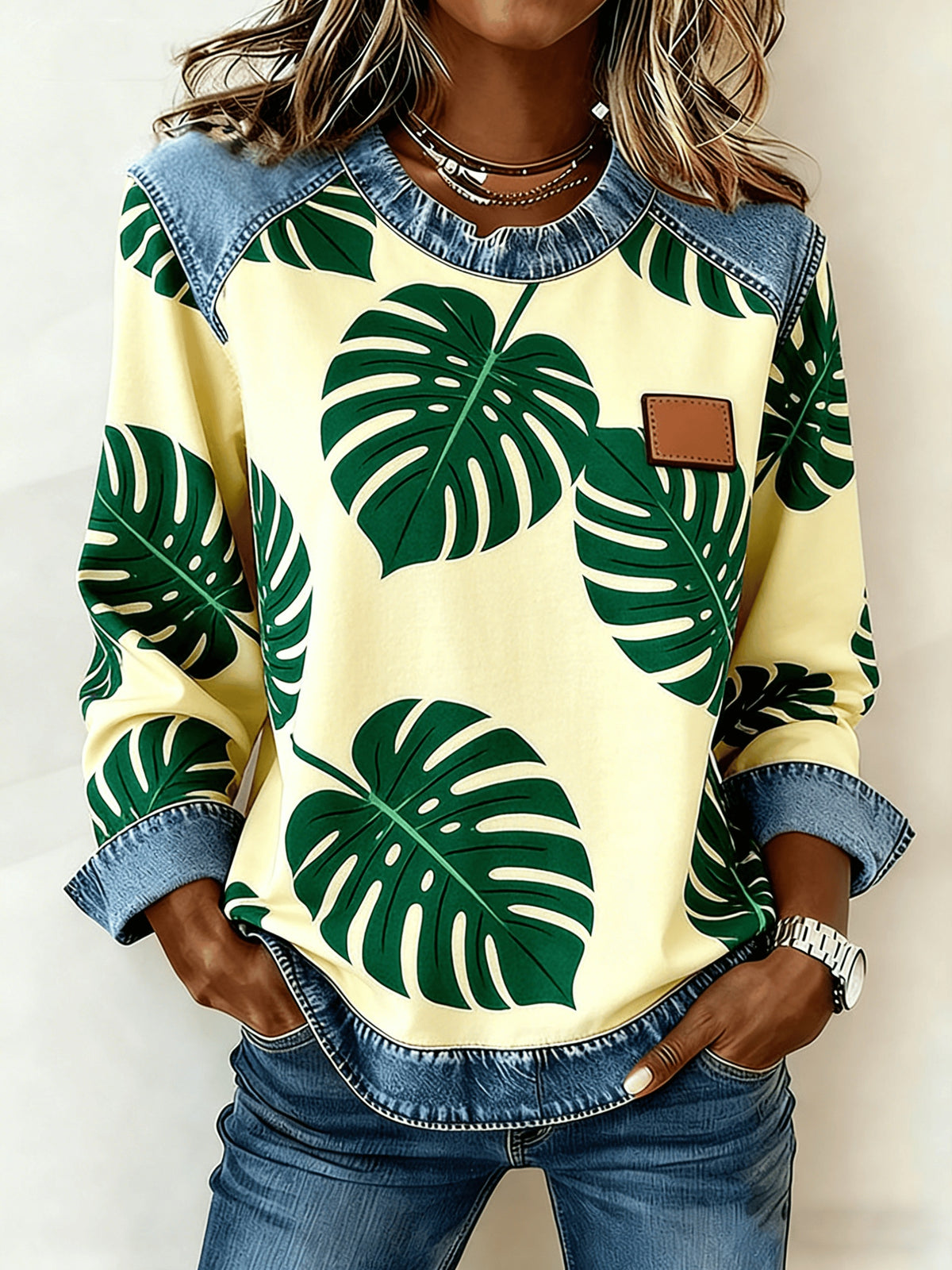 Women's patchwork denim sweatshirt with pale yellow base and bold green Monstera leaf print; denim yoke and cuffs.