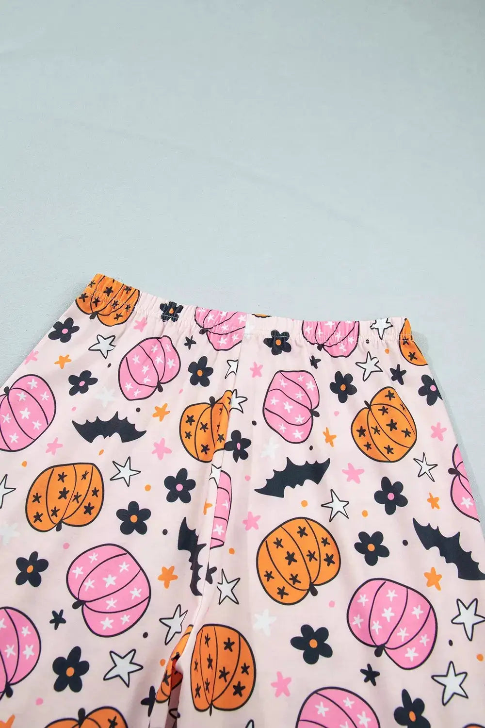 Halloween pumpkin-print lounge pants on pink fabric with orange and pink pumpkins, bats, and stars