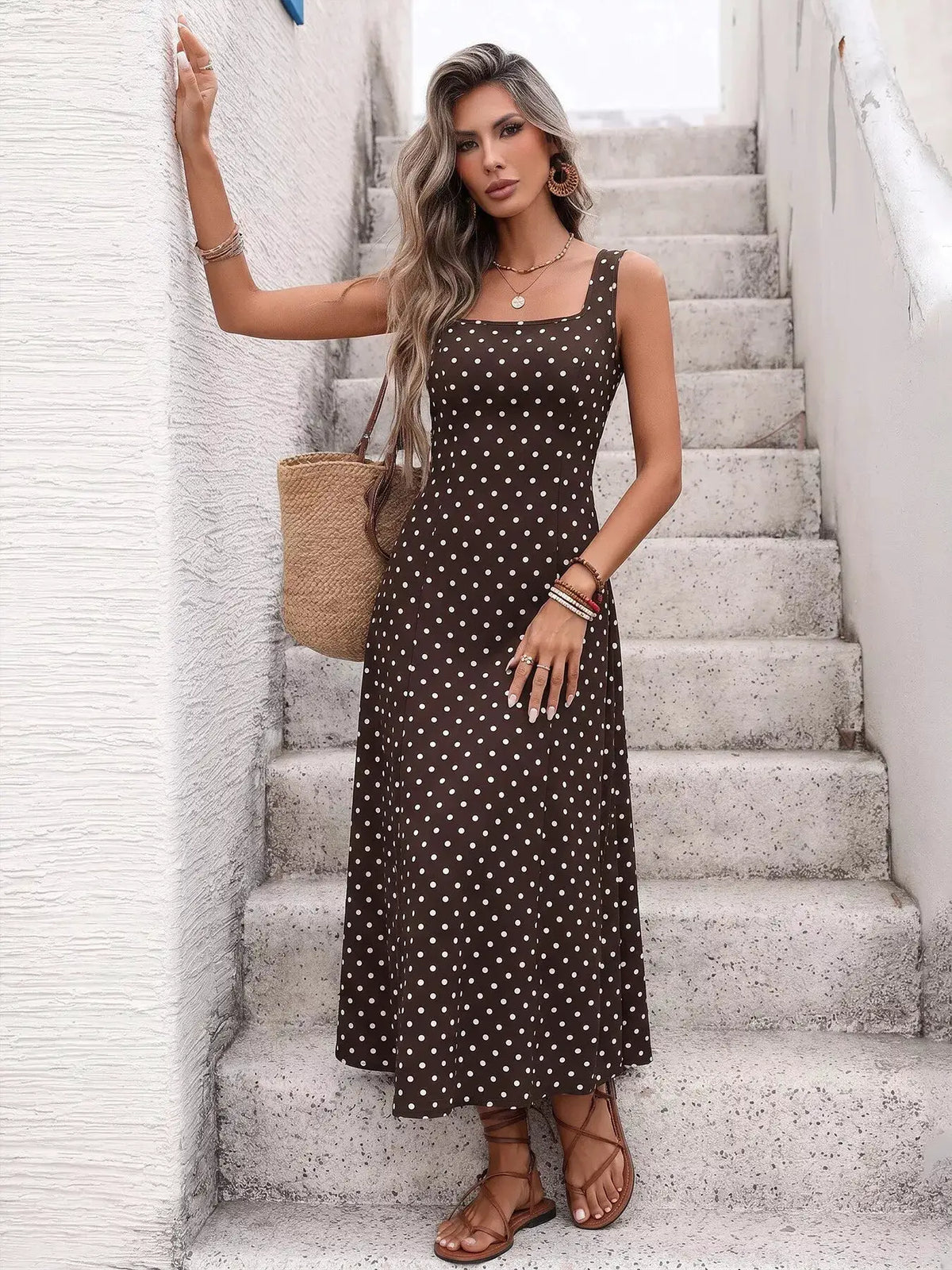Polka dot sleeveless maxi dress in brown with white dots; worn with a straw tote and sandals