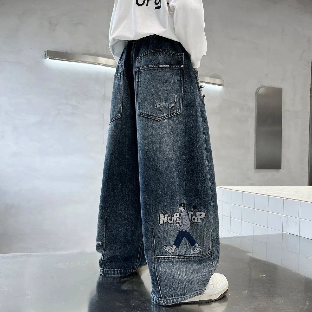 Trendy Boys Straight Wide Leg Denim Jeans; dark blue denim with rear pocket and cartoon graphic patch.