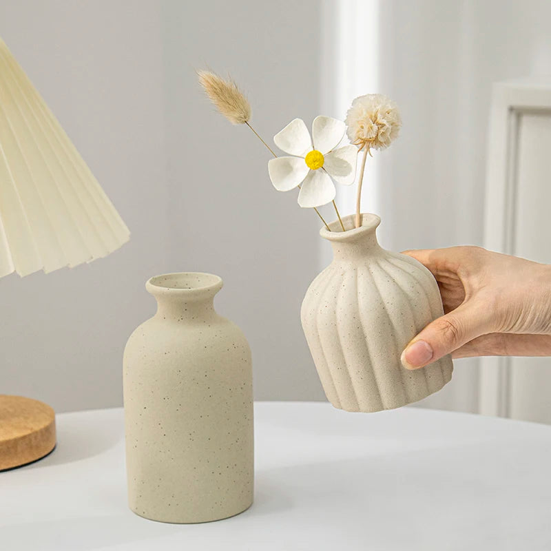 Ceramic flower vase set: two beige vases, ribbed vase held by hand with dried flowers, smooth speckled vase beside.