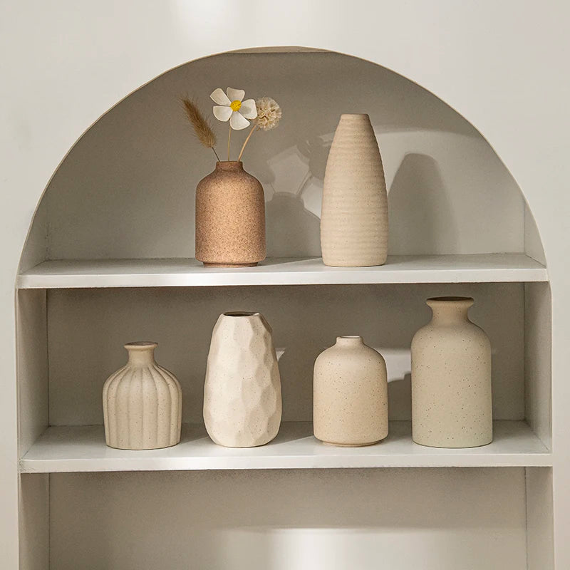 Ceramic vase set on white shelf with neutral beige tones, speckled and faceted shapes and a dried-flower arrangement.