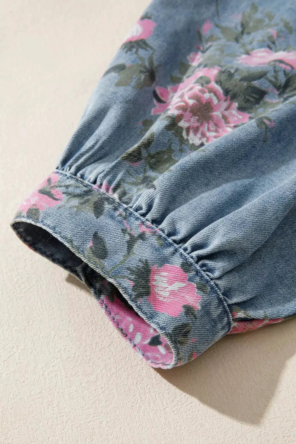 Floral print denim button-up shirt sleeve close-up with pink flowers on blue fabric