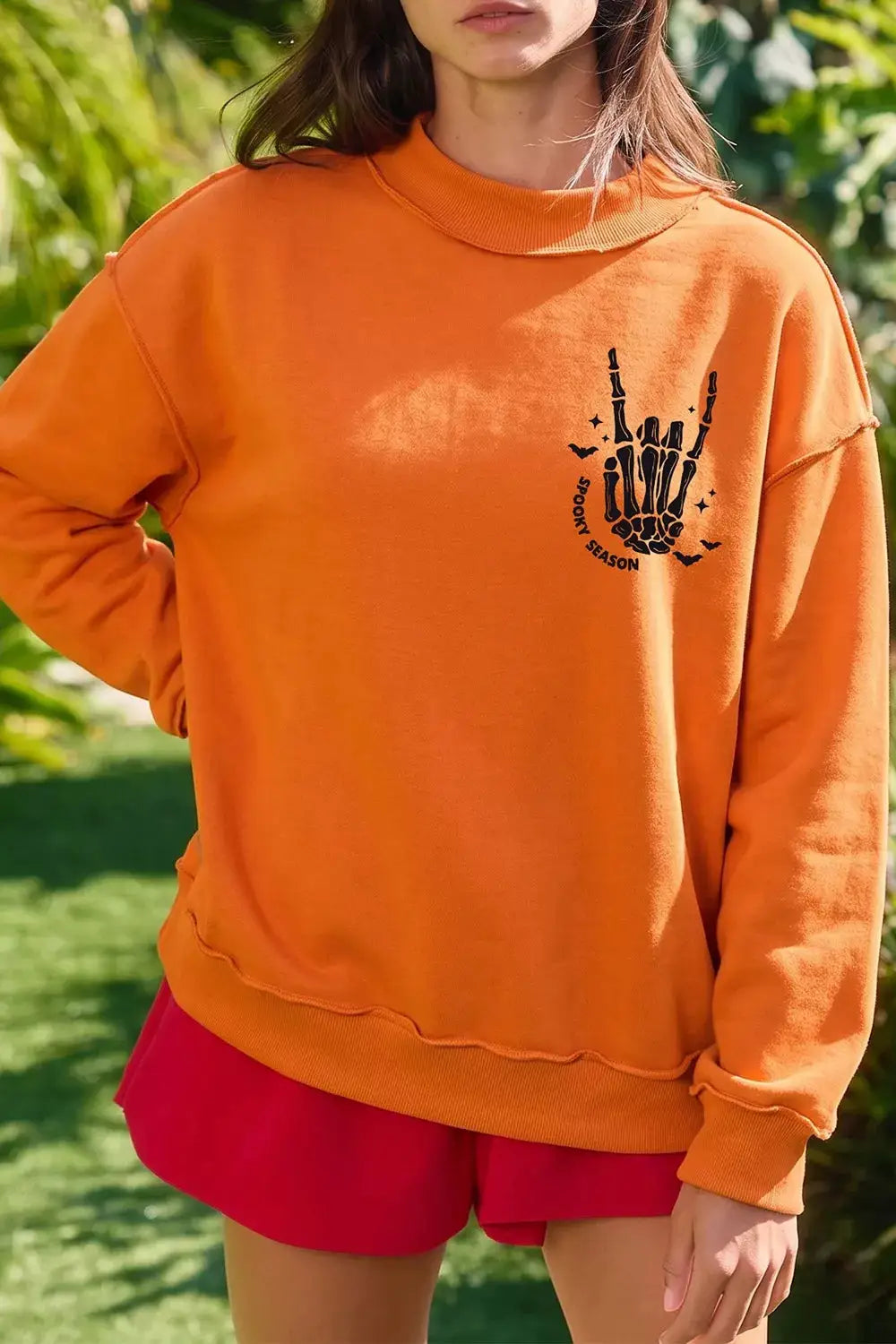 Spooky Season mock neck reversible Halloween sweatshirt in orange with black skeleton hand graphic.