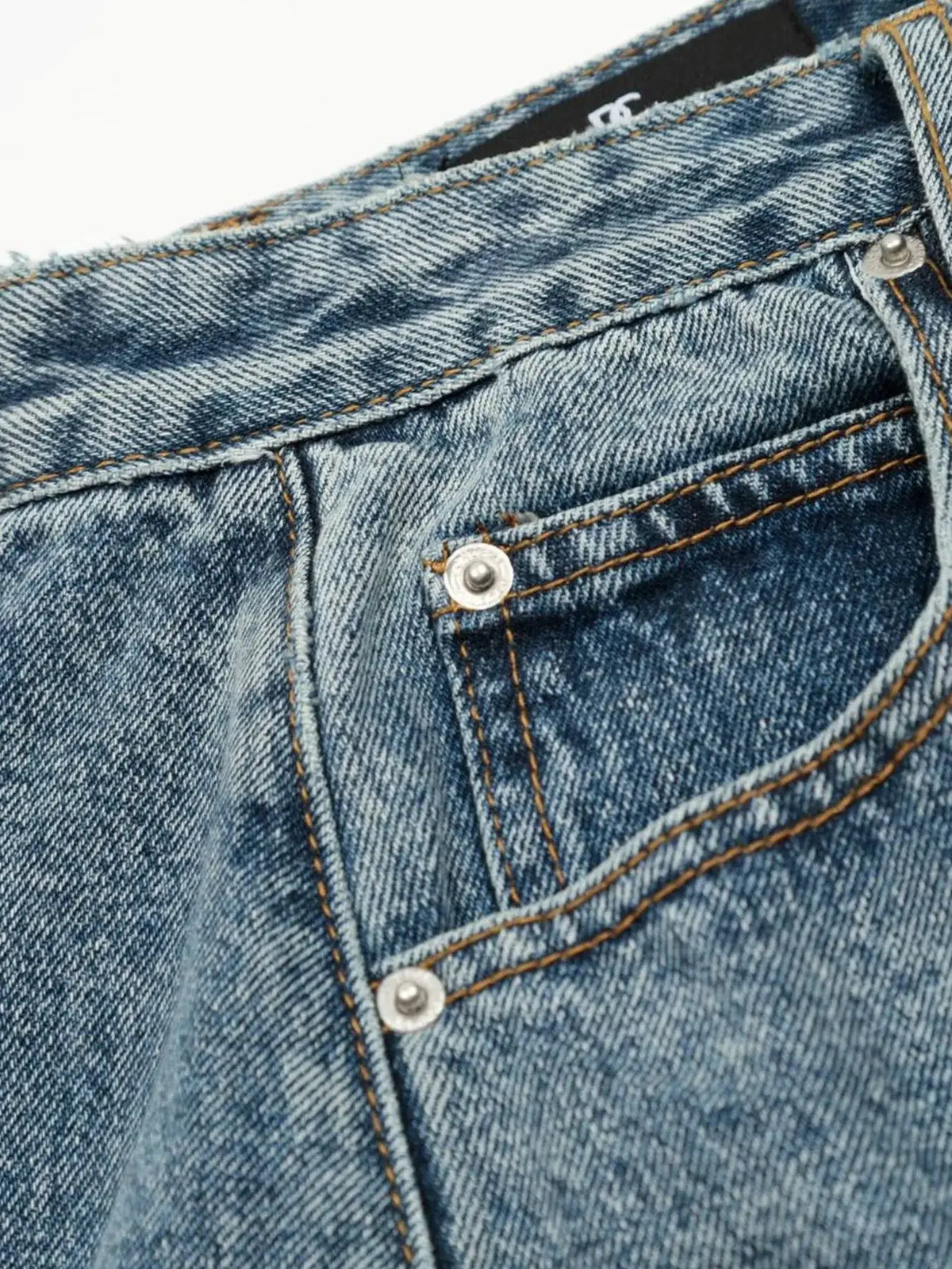 Men's washed denim shorts; close-up of blue denim with silver rivets and orange stitching.