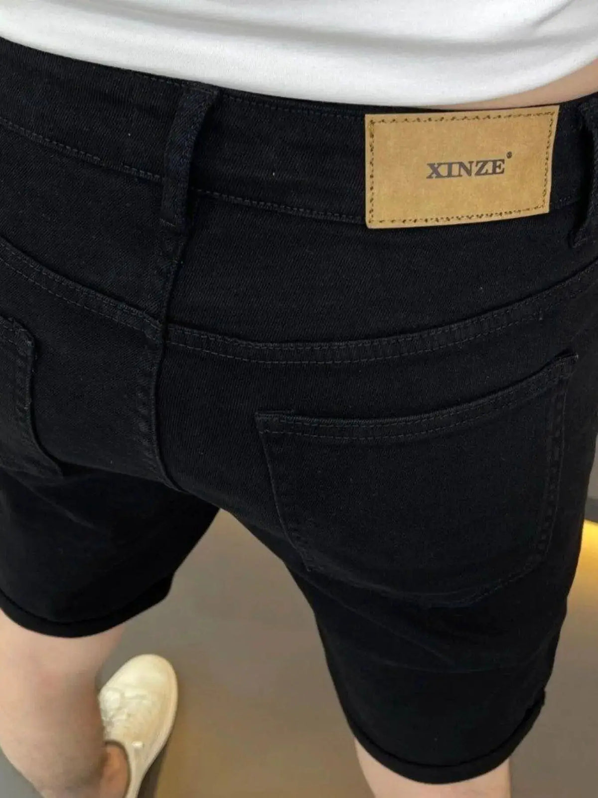 Men's black cotton-stretch denim shorts with pockets and belt loops; XNZE patch on back waistband.