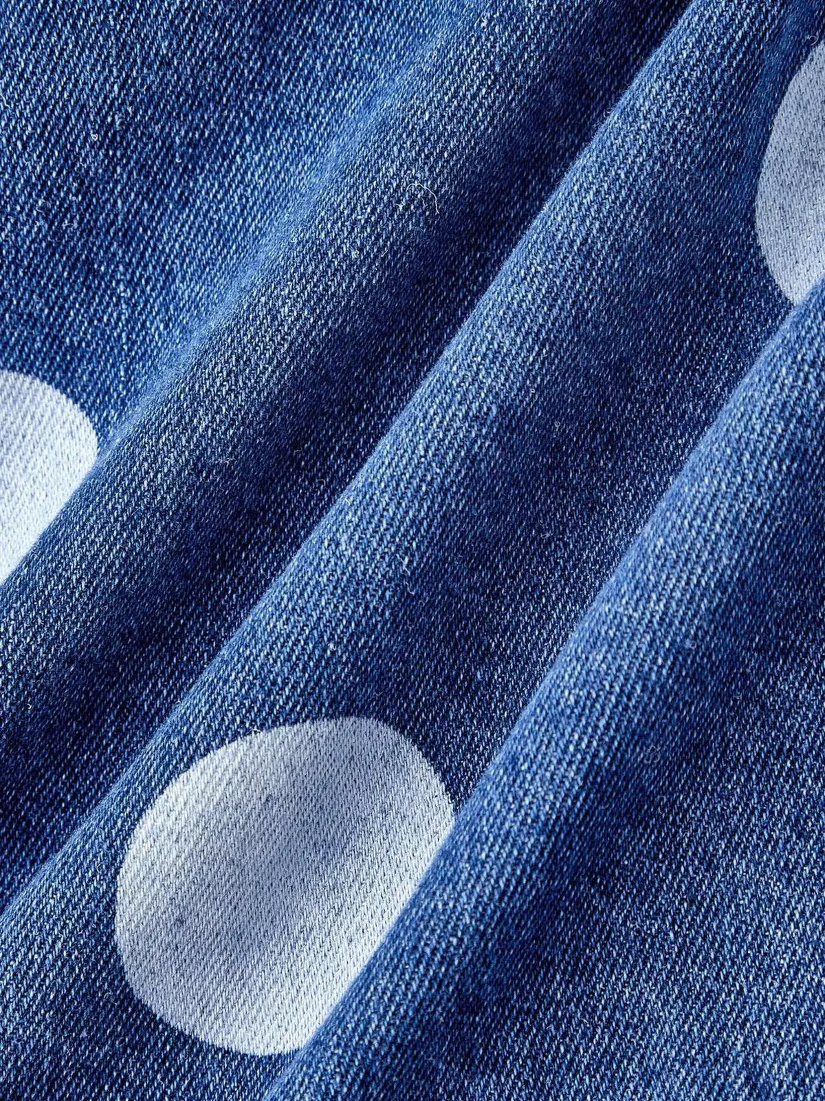 Women's cropped denim jacket with white polka dots, blue wash, open front.
