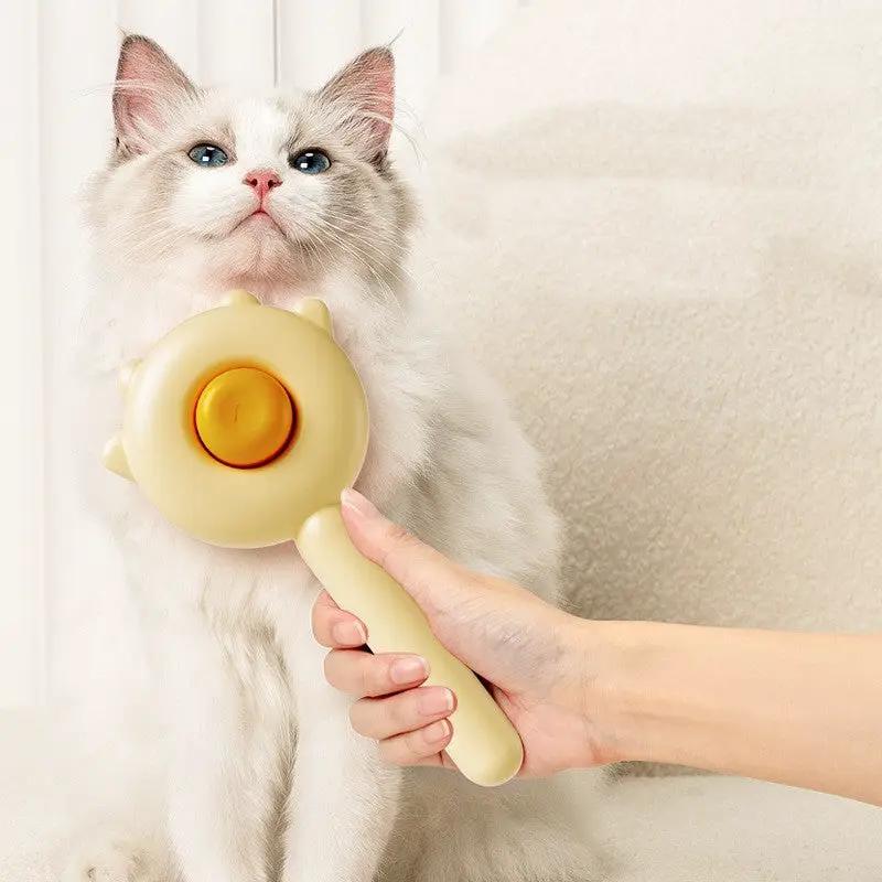 Cat grooming massager brush in cream with orange center, shown on a fluffy white cat.