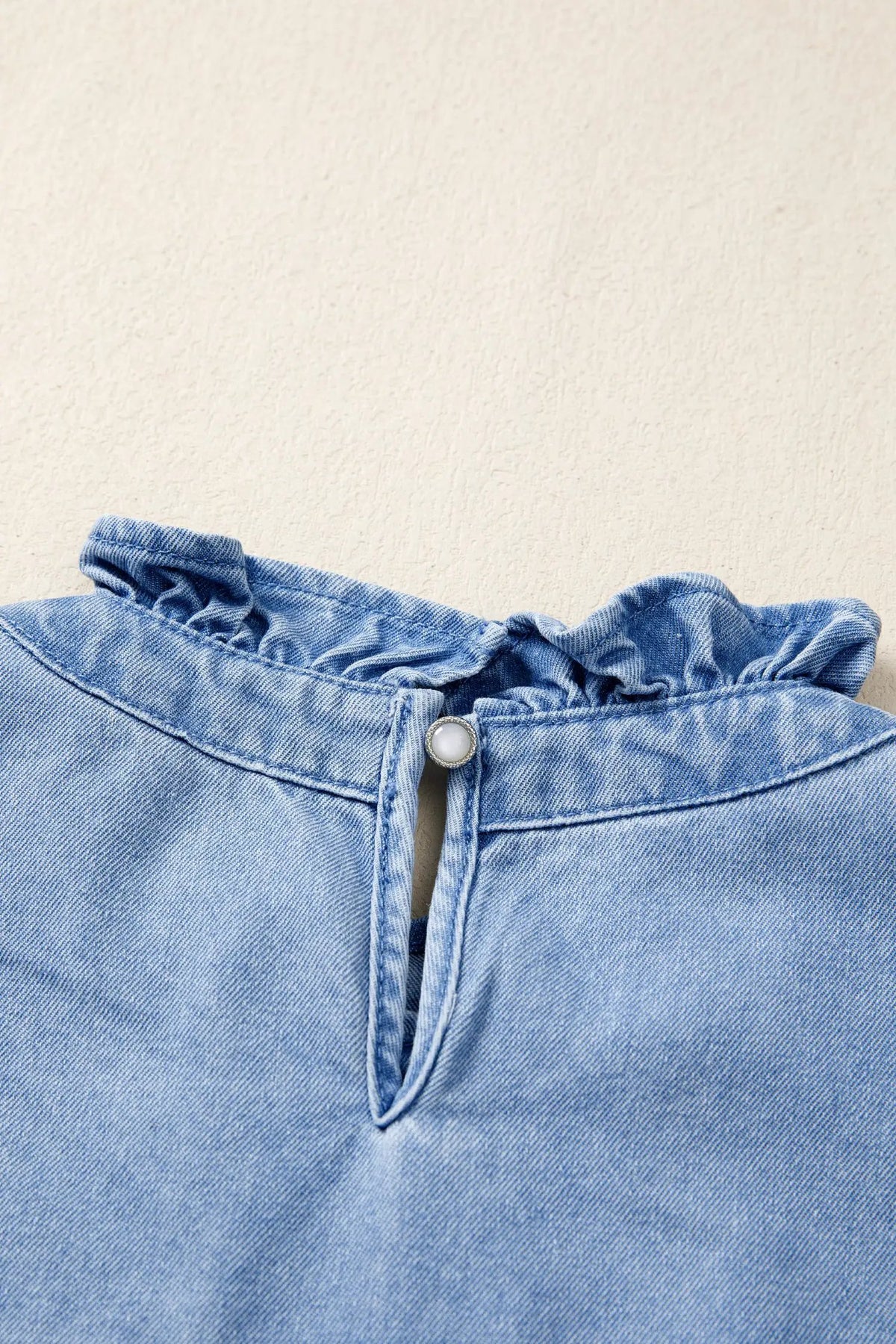 Distressed denim top with frill collar and wide flutter sleeves in light wash.