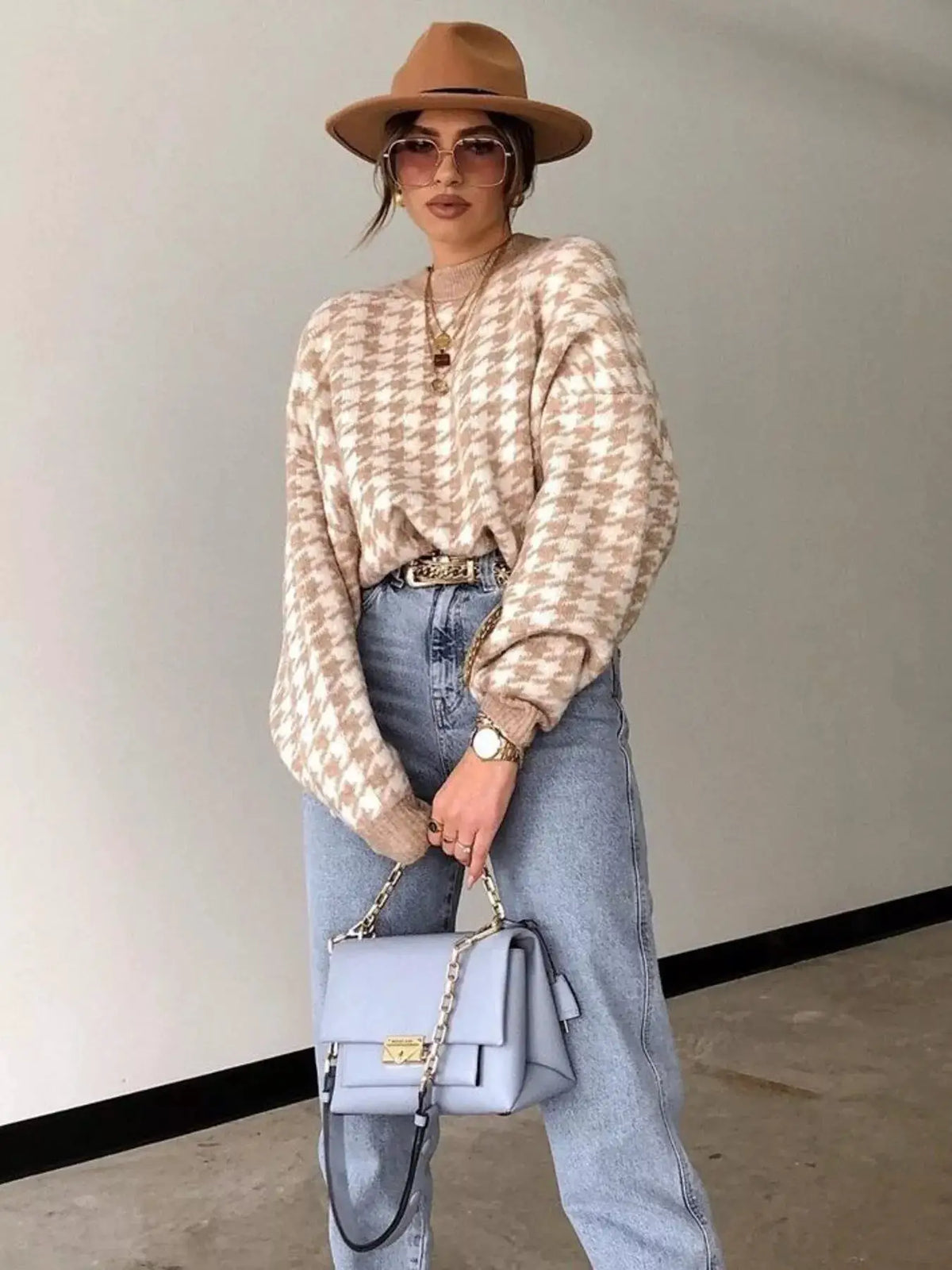 Classic oversized houndstooth sweater in beige/cream, styled with light-wash jeans, tan hat, and light blue handbag