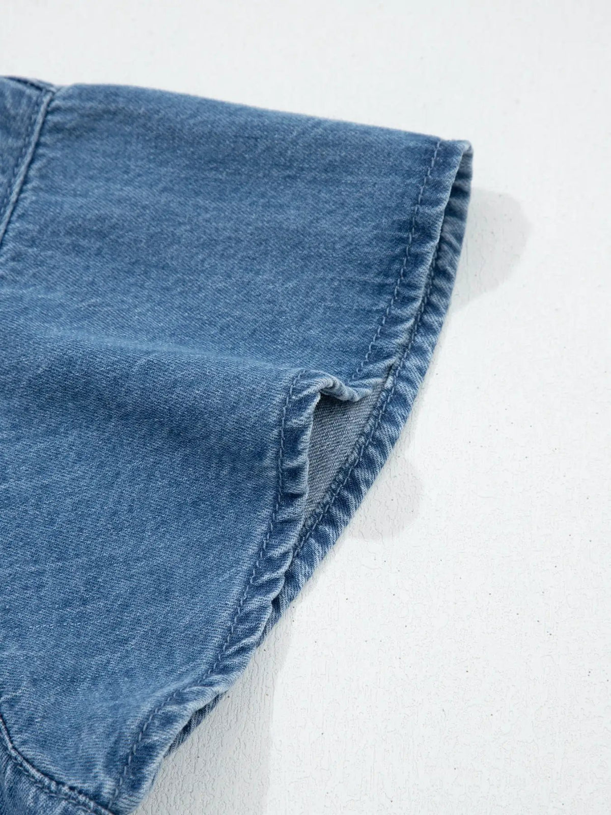 Women's denim button-up blouse by Trendsi in blue denim; close-up of short sleeve hem.