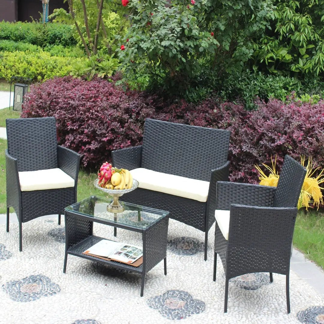 4 pc black rattan patio furniture set with beige cushions and glass coffee table.