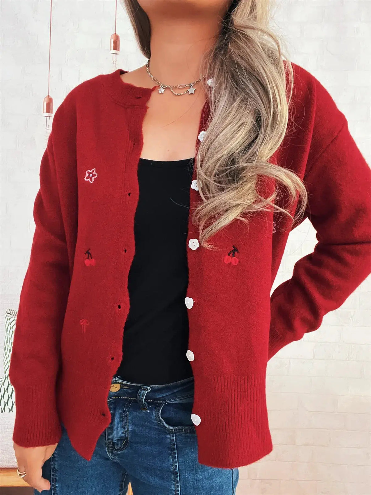 Red ribbed knit cardigan with button-front closure and cherry embroidery, worn over a black top.