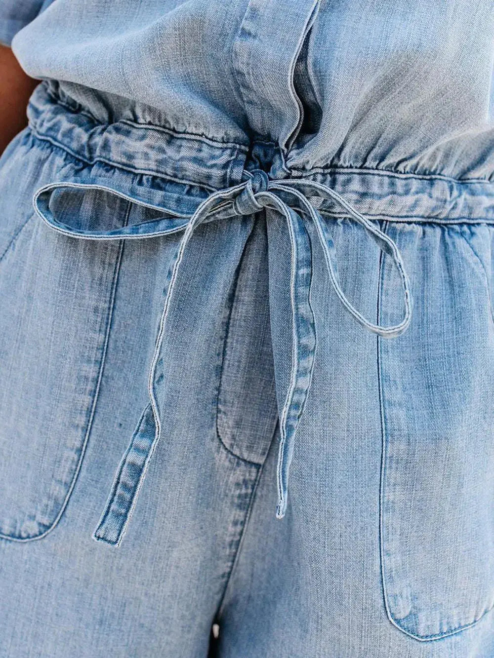 Denim romper with half sleeves, tie waist, and pockets; light blue wash