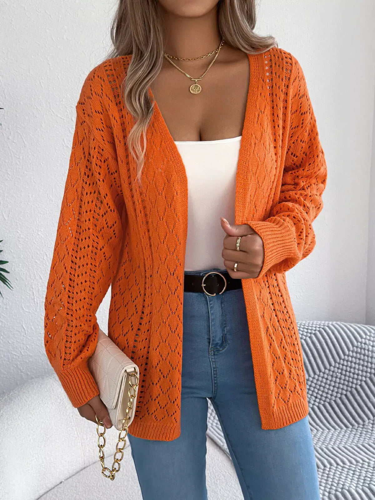 Openwork orange long-sleeve cardigan with open-front stretch knit, worn over a white top paired with blue jeans
