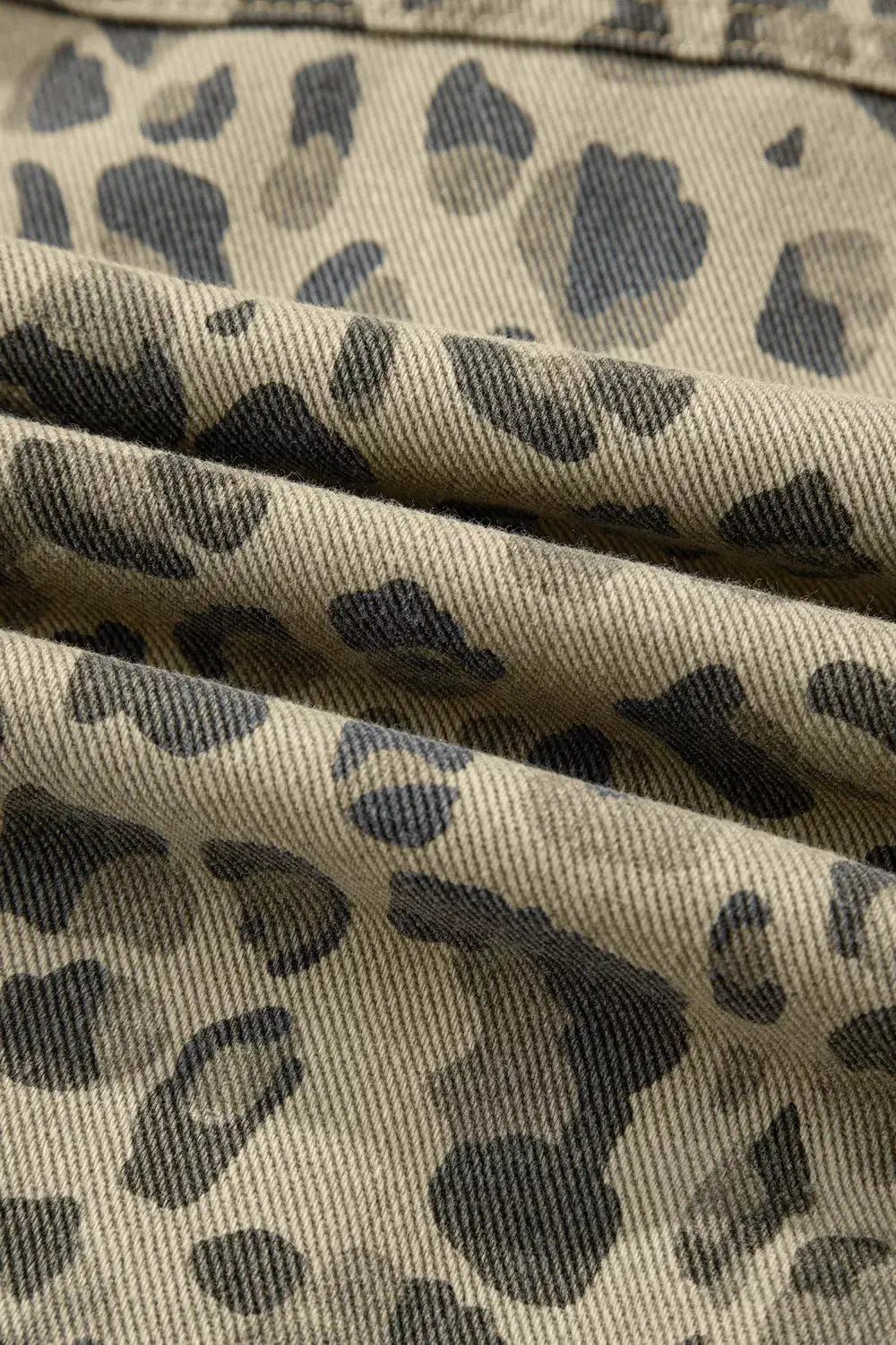 Leopard print denim jacket fabric close-up; beige cotton blend with dark spots.