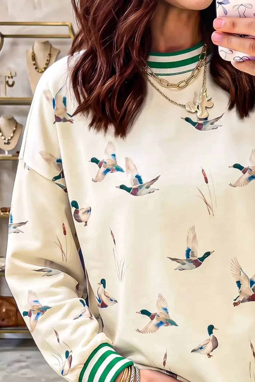 Whimsical duck-print sweatshirt in cream with green striped trim at neck and cuffs.