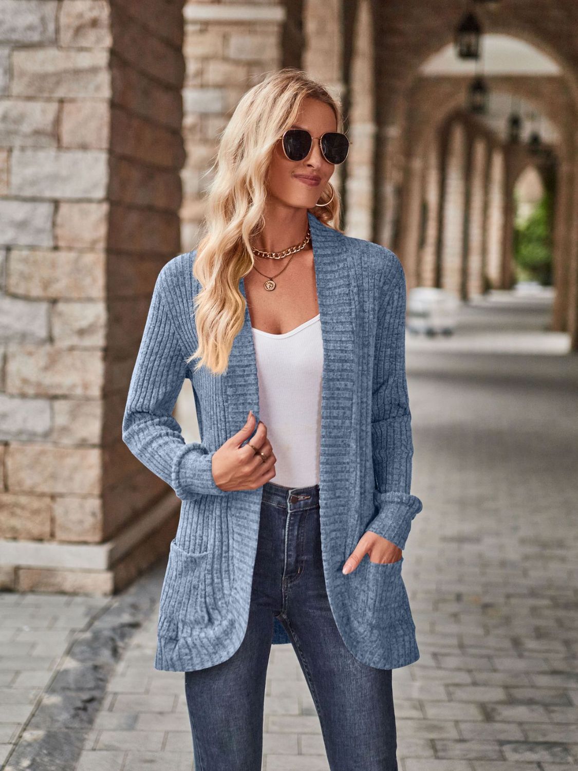 Stretchy open-front cardigan with deep side pockets in light blue, ribbed knit worn over a white top with jeans.
