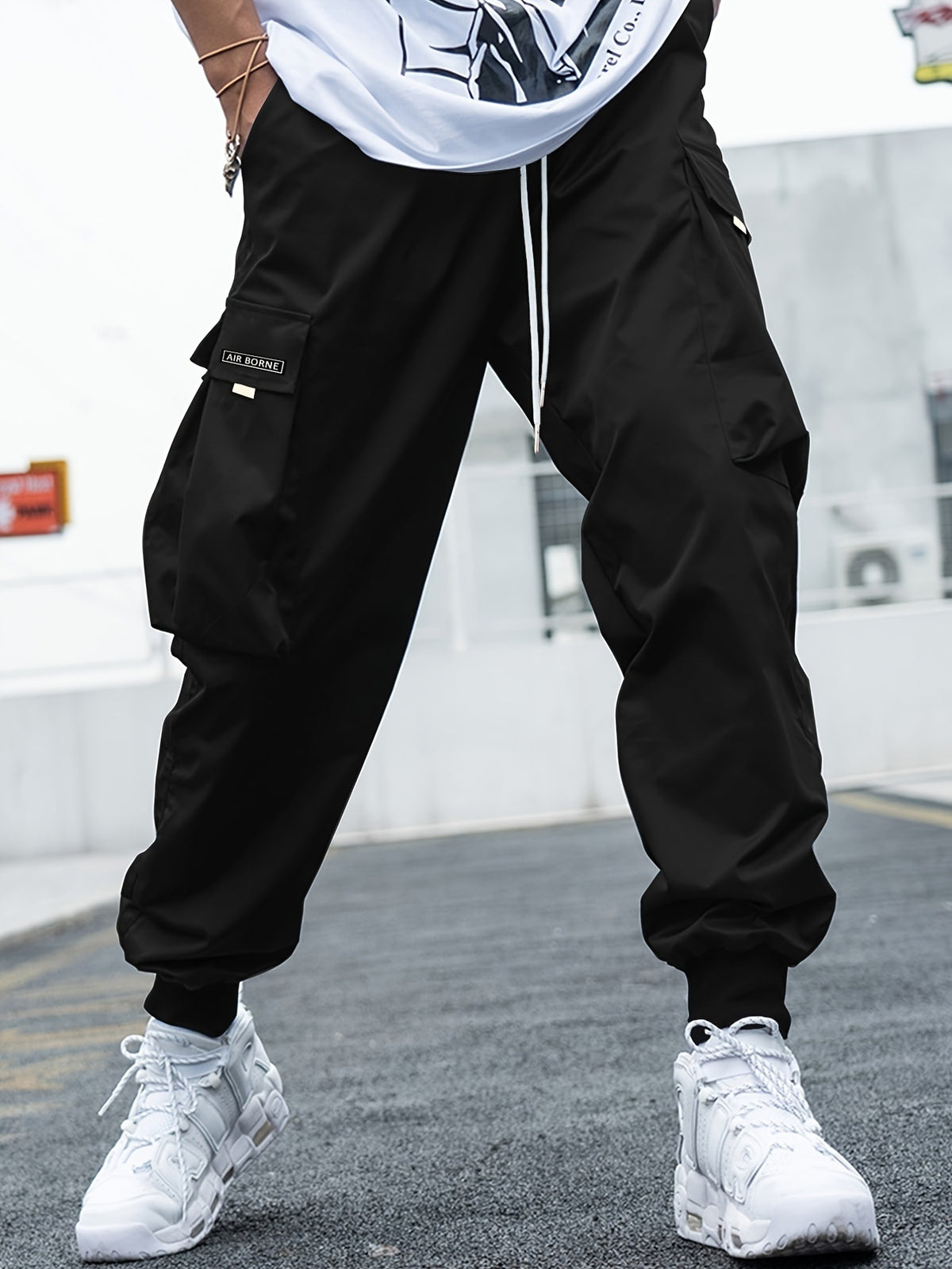 Men's black cargo pants with multiple pockets and drawstring waist; Air Borne patch on cargo pocket.