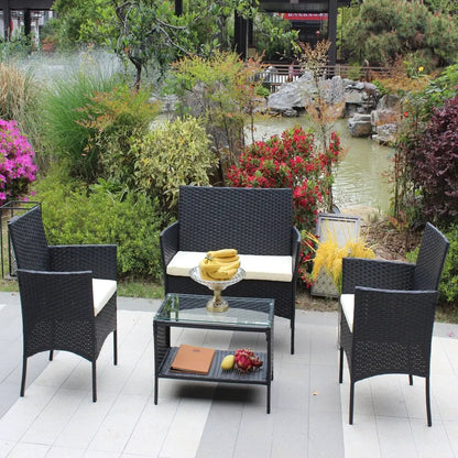 4 pc rattan patio furniture set in black with cream cushions; includes four chairs and a glass-top coffee table.