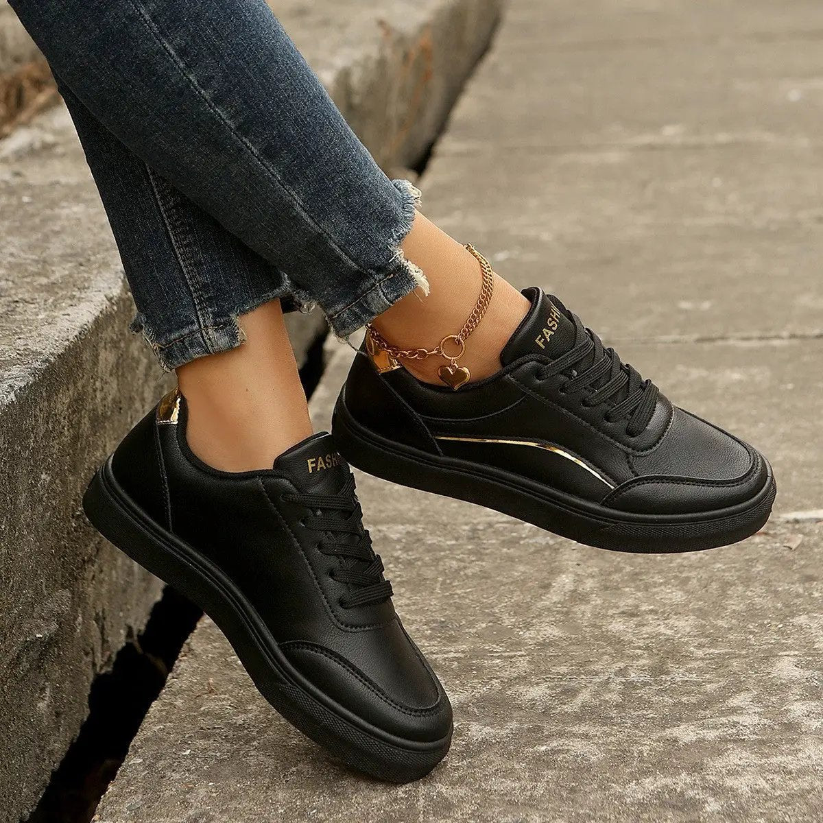 AdTec black lace-up sneakers with thick sole and gold stripe, worn with distressed jeans.
