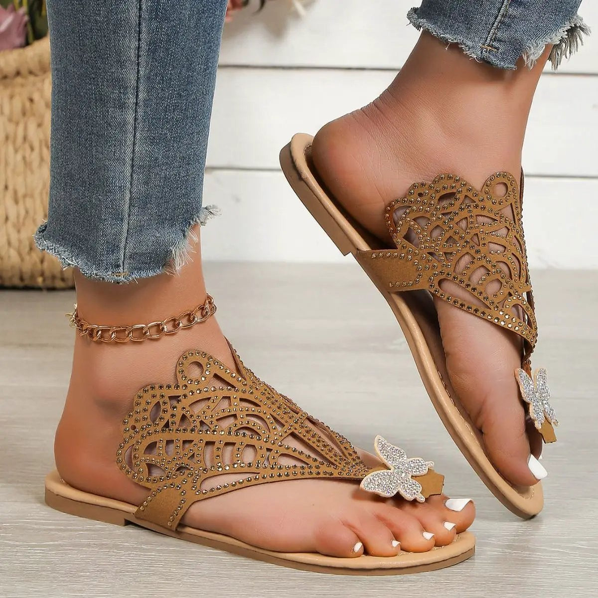 Pair of tan rhinestone-embellished slip-on sandals with hollow lattice cutouts and butterfly accents.