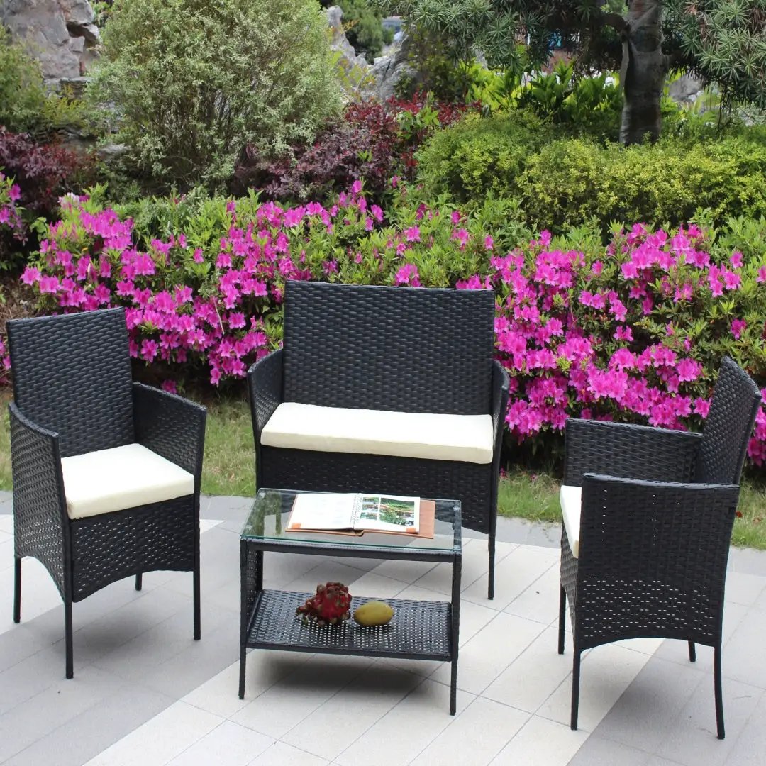 4-piece rattan patio furniture set in black wicker with cream cushions; includes loveseat, two armchairs, and glass-top coffee table