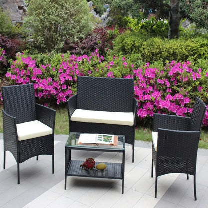 4-piece rattan patio furniture set in black wicker with cream cushions; includes loveseat, two armchairs, and glass-top coffee table