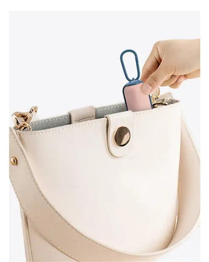 Portable poop bag dispenser inside a beige handbag with pink and blue accents.